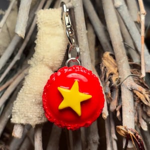 Peut inclure: Un charm en forme d'&eacute;toile rouge et jaune avec un fermoir argent&eacute;. Le charm pr&eacute;sente une &eacute;toile jaune vif sur un fond rouge. Le charm est attach&eacute; &agrave; un fermoir argent&eacute;, pr&ecirc;t &agrave; &ecirc;tre ajout&eacute; &agrave; un porte-cl&eacute;s ou un collier.