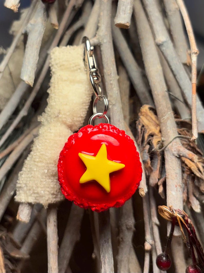 Peut inclure: Un charm en forme d'&eacute;toile rouge et jaune avec un fermoir argent&eacute;. Le charm pr&eacute;sente une &eacute;toile jaune vif sur un fond rouge. Le charm est attach&eacute; &agrave; un fermoir argent&eacute;, pr&ecirc;t &agrave; &ecirc;tre ajout&eacute; &agrave; un porte-cl&eacute;s ou un collier.