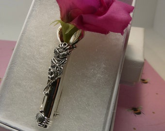 Puede incluir: Broche de plata con un diseño de rosa detallado. La broche tiene forma de tallo con hojas y una rosa en la parte superior. La broche está en una caja blanca con una flor rosa.