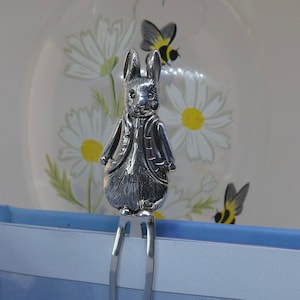 Puede incluir: Marcapáginas de plata con una figura de conejo detallada. El conejo está de pie con los brazos cruzados y tiene un aspecto texturizado y realista.