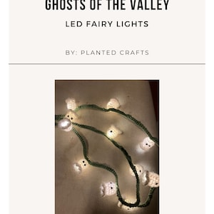 Puede incluir: Una cadena de luces LED de hadas con cubiertas de crochet en forma de fantasma. Las luces son blancas y los fantasmas son blancos con detalles verdes. El texto "GHOSTS OF THE VALLEY LED FAIRY LIGHTS BY: PLANTED CRAFTS" es visible en la parte superior de la imagen.