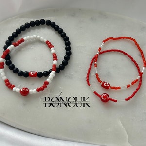 Puede incluir: Dos pulseras de cuentas con cuentas rojas, blancas y negras. Cada pulsera tiene un dije con la bandera turca.