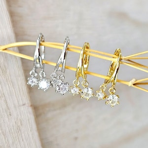 Può includere: Tre paia di orecchini pendenti con un gruppo di tre pietre di zircone cubico trasparenti su ogni orecchino. Gli orecchini sono disponibili in argento e oro.