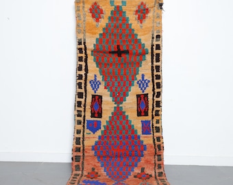 May include: A long, narrow rug with a geometric pattern in shades of red, blue, green, and black on a beige background. The rug has a fringe on the bottom edge.