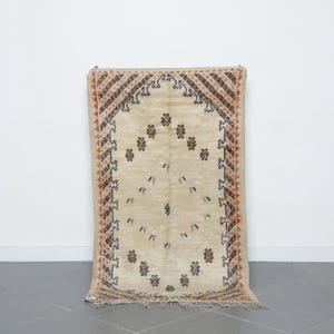 a beige rug with intricate patterns and designs, placed on a gray tiled floor against a white wall.