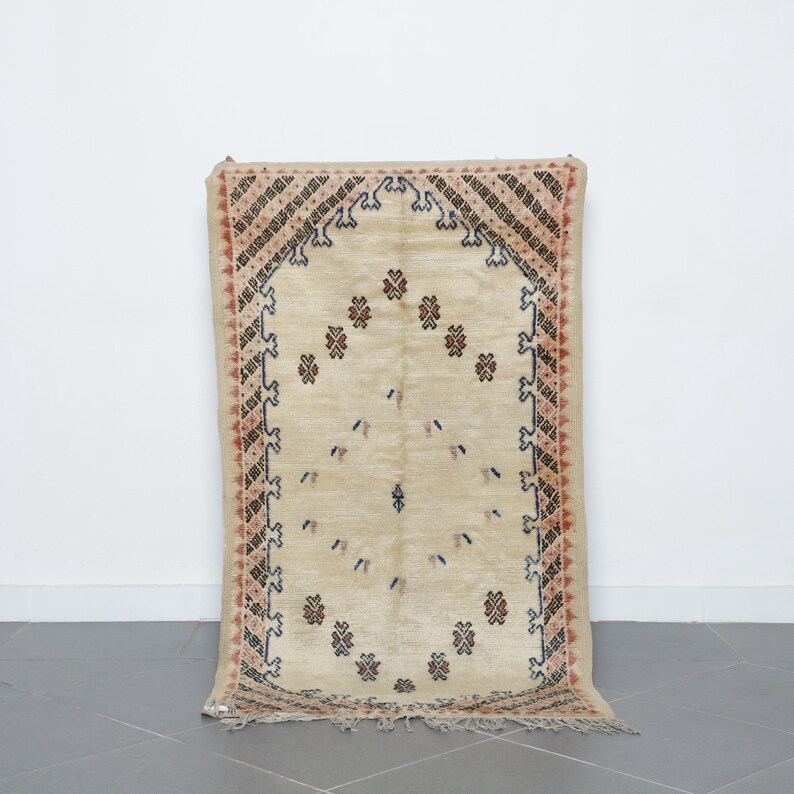 a beige rug with intricate patterns and designs, placed on a gray tiled floor against a white wall.
