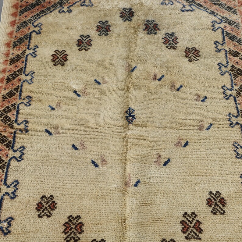 a close-up view of a beige rug with intricate patterns and designs, including small floral motifs and geometric shapes.