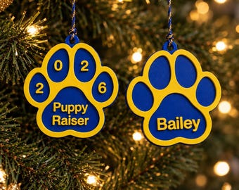 May include: Two blue and yellow paw-shaped ornaments hanging from blue and gold cords. The left ornament features the text 0 2 2 6 and Puppy Raiser. The right ornament features the text Bailey. Both ornaments have a layered design.