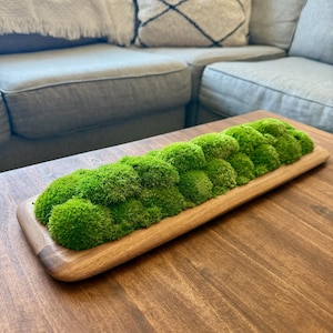 Puede incluir: Una bandeja de madera larga y rectangular llena de musgo verde preservado. La bandeja está sobre una mesa de madera.