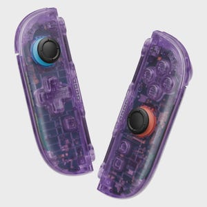 Puede incluir: Dos mandos de juego morados transparentes. Los mandos tienen joysticks negros con detalles azules y naranjas. El circuito interno es visible a trav&eacute;s de la carcasa transparente. Los mandos est&aacute;n dise&ntilde;ados para una consola de juegos.