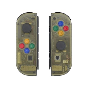 May include: Two transparent yellow game controllers with black joysticks and colored buttons. The controllers have a clear design, revealing internal components. The buttons are red, blue, green, and yellow.