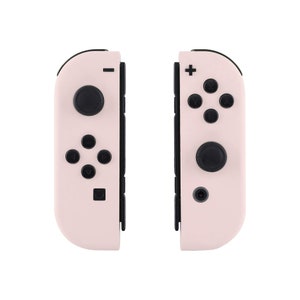 May include: A pair of pink Nintendo Switch Joy-Con controllers with black buttons and a black border. The controllers are separated and show the front view.