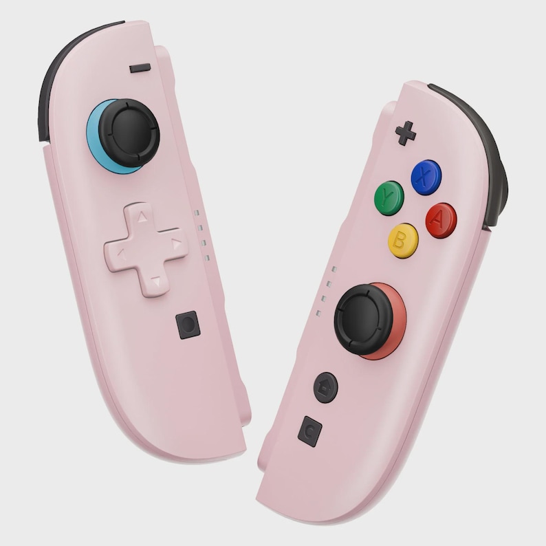 May include: Two pink game controllers with black accents. One controller has a directional pad and a blue joystick. The other controller has colored buttons and a red joystick. The controllers are designed for gaming.