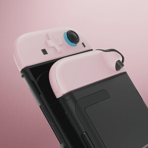 May include: A pink and black gaming controller with a D-pad, buttons, and a joystick. The controller has a sleek design with a black body and pink accents. The joystick has a blue ring around it.