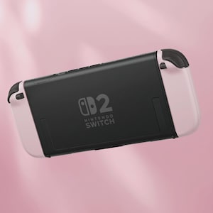 May include: A Nintendo Switch console in a soft pink and black color scheme. The back of the console is black with the Nintendo Switch logo and the number "2" printed on it. The sides are a light pink color.