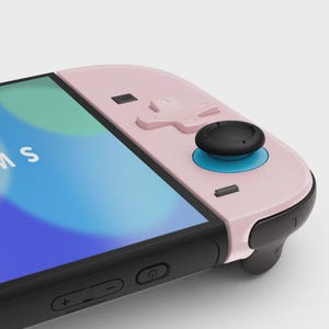 May include: A close-up of a pink and black game controller. The controller has a black joystick with a blue ring, a directional pad, and several buttons. The screen displays a blue and white image.