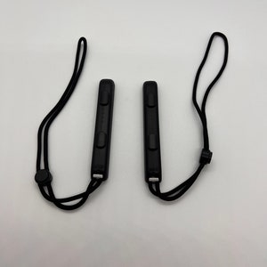 Puede incluir: Dos mandos negros Nintendo Switch Joy-Con con correas de mu&ntilde;eca negras. Los mandos tienen botones y un punto de fijaci&oacute;n de correa negro.