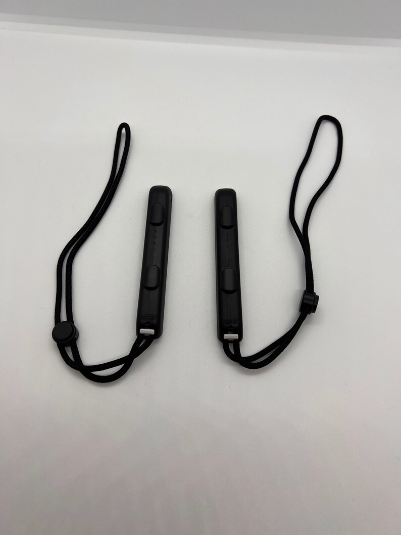 Puede incluir: Dos mandos negros Nintendo Switch Joy-Con con correas de mu&ntilde;eca negras. Los mandos tienen botones y un punto de fijaci&oacute;n de correa negro.