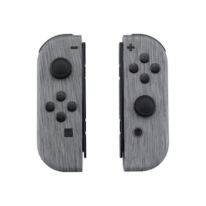 Może przedstawiać: Para kontroler&oacute;w Nintendo Switch Joy-Con w kolorze szarym i czarnym z wzorem imitującym drewno.