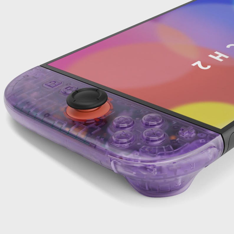 Puede incluir: Primer plano de un mando de juego transparente p&uacute;rpura con botones negros y un joystick negro. La pantalla muestra un dise&ntilde;o abstracto colorido. El mando tiene un dise&ntilde;o elegante y moderno.