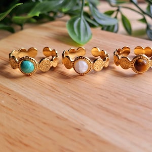 May include: Four gold rings with different colored gemstones. The rings are made of a textured metal and have a scalloped edge. The gemstones are turquoise, white, tiger's eye, and lapis lazuli.