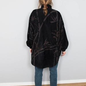 Puede incluir: Chaqueta negra de gran tama&ntilde;o con cuello alto y un estampado de hojas de bamb&uacute; en tonos marrones. La chaqueta se lleva sobre unos vaqueros azules y zapatillas blancas.