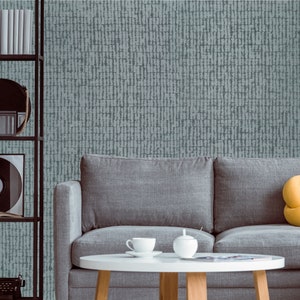 May include: A gray couch with a yellow pillow sits in front of a wall with a blue and white patterned wallpaper. A small round table with a white surface sits in front of the couch. There are two white teacups and a white sugar bowl on the table.