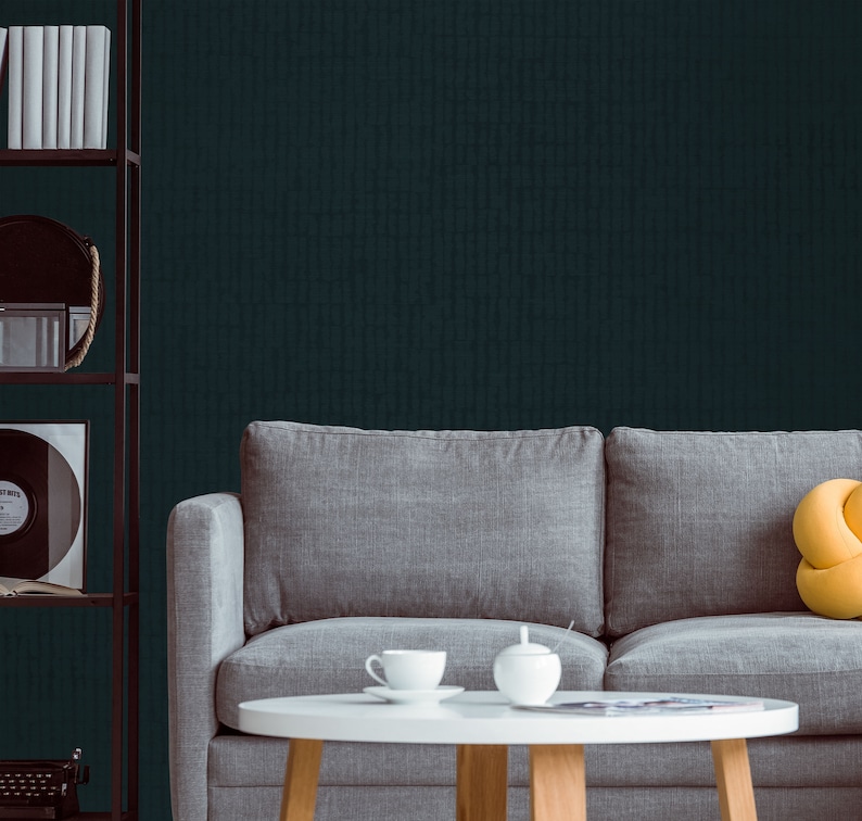 May include: A gray sofa with a yellow throw pillow sits in front of a dark teal wall. A white coffee table with a teacup and saucer and a sugar bowl sits in front of the sofa.