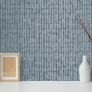 May include: A blue and white patterned wallpaper with a subtle texture. The wallpaper is displayed in a room with a picture frame, a cactus in a white pot, and a vase with branches.