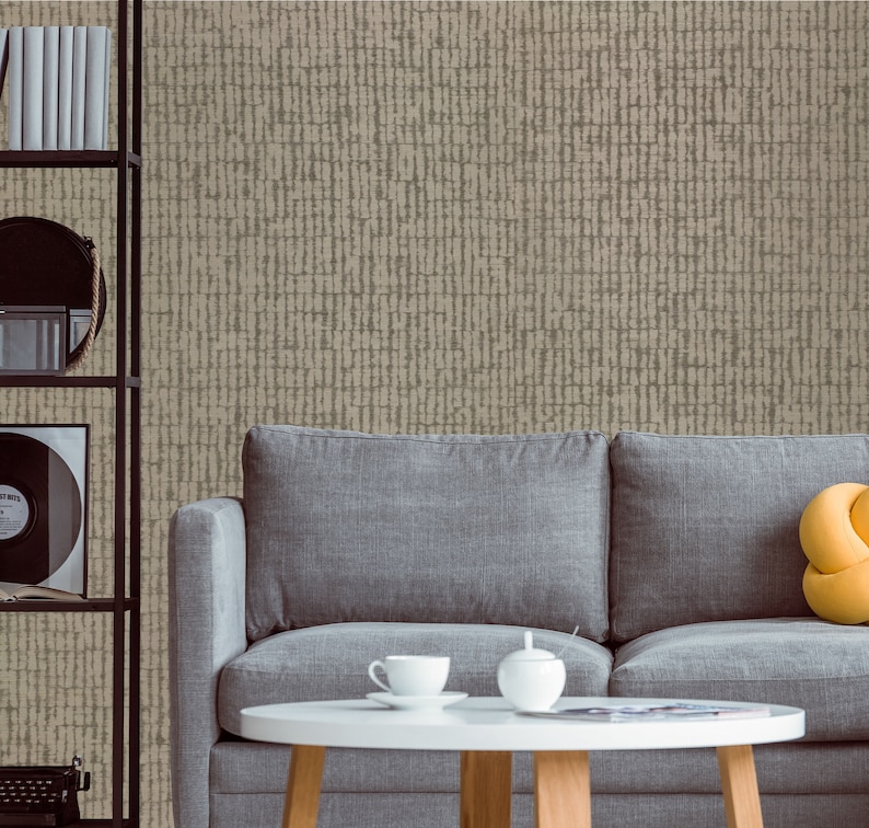 May include: A gray fabric sofa with a yellow throw pillow sits in front of a wall with a beige textured wallpaper. A small round table with a white top and wooden legs sits in front of the sofa. There are two white ceramic cups and a white ceramic sugar bowl on the table.