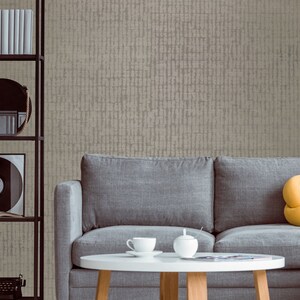May include: A gray sofa with a yellow pillow sits in front of a wall with a textured beige wallpaper. A white coffee table with a cup and saucer and a sugar bowl sits in front of the sofa.