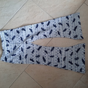 Puede incluir: Un pantal&oacute;n de campana con base blanca y un patr&oacute;n repetitivo de color azul oscuro que muestra plumas y formas geom&eacute;tricas de diamante. El pantal&oacute;n tiene una cintura ajustada y se ensancha notablemente hacia el dobladillo inferior.
