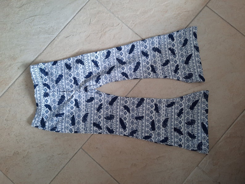 Puede incluir: Un pantal&oacute;n de campana con base blanca y un patr&oacute;n repetitivo de color azul oscuro que muestra plumas y formas geom&eacute;tricas de diamante. El pantal&oacute;n tiene una cintura ajustada y se ensancha notablemente hacia el dobladillo inferior.