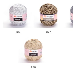 Op de afbeelding: Vijf bollen garen in verschillende kleuren, waaronder goud, zilver en bruin. Elke bol heeft een label met de tekst "YarnArt BRIGHT".