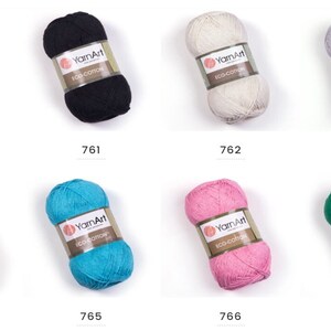 Peut inclure: Sept pelotes de fil YarnArt Eco Cotton dans diff&eacute;rentes couleurs, notamment blanc, noir, beige, gris, jaune, turquoise, rose et vert. Chaque pelote porte une &eacute;tiquette avec le nom de la marque "YarnArt" et le texte "Eco Cotton".