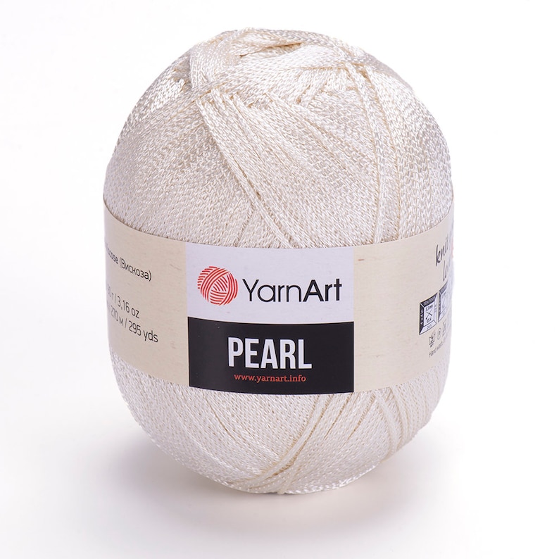 Puede incluir: Un ovillo de hilo blanco YarnArt Pearl. La etiqueta dice "YarnArt Pearl" y "www.yarnart.info".