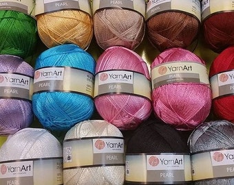 Op de afbeelding: Assortiment van 12 spoelen YarnArt Pearl garen in verschillende kleuren, waaronder groen, goud, bruin, blauw, roze, wit, zwart en grijs. Elke spoel heeft een label met de merknaam en het woord "Pearl".