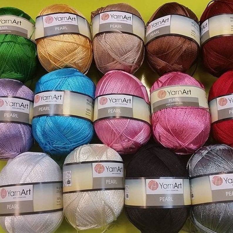 Puede incluir: Surtido de 12 carretes de hilo YarnArt Pearl en varios colores, incluyendo verde, dorado, marr&oacute;n, azul, rosa, blanco, negro y gris. Cada carrete tiene una etiqueta con el nombre de la marca y la palabra "Pearl".