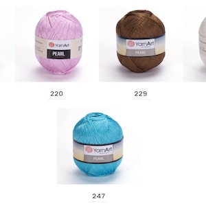 Puede incluir: Cinco ovillos de hilo en diferentes colores: beige, rosa, marr&oacute;n, blanco y turquesa. Cada ovillo tiene una etiqueta que dice "YarnArt PEARL".