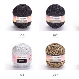 Op de afbeelding: Assortiment van tien bollen garen in verschillende kleuren, waaronder goud, zilver, zwart en bruin. Elke bol heeft een label met de tekst "YarnArt BRIGHT".
