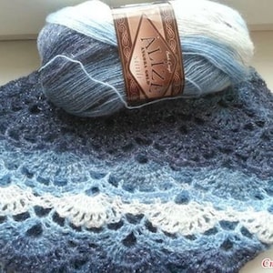 May include: A blue, white, and gray ombre yarn ball with a label that reads "Alize Angel Gold Simli" in a brown and gold design. The yarn is used to crochet a blue and white ombre shawl with a lacy pattern.