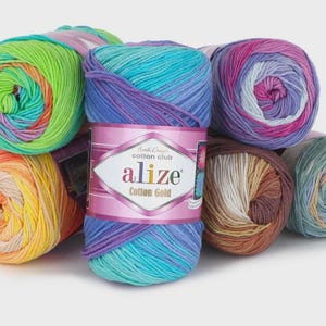 Könnte beinhalten: Eine Auswahl an bunten Alize Cotton Gold Garnknäueln. Das Garn ist in verschiedenen Grüntönen, Blau, Lila, Rosa, Orange, Gelb und Braun gehalten. Auf dem Garn steht "alize Cotton Gold".