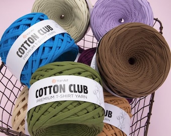 May include: A basket filled with six different colors of cotton t-shirt yarn. The yarn is labeled "Cotton Club Premium T-Shirt Yarn".