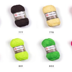 Peut inclure: Huit pelotes de fil YarnArt Eco Cotton dans diff&eacute;rentes couleurs, dont le rouge, le marron, le jaune, l'orange, le vert et le rose. Chaque pelote est &eacute;tiquet&eacute;e avec le nom de la marque et le num&eacute;ro de la couleur.