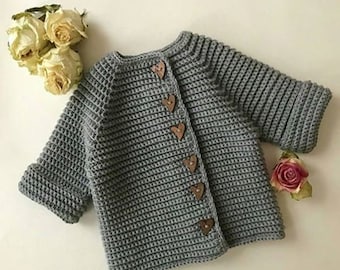 May include: A gray crocheted cardigan with a round neckline and heart-shaped buttons. The cardigan has long sleeves and a ribbed texture.