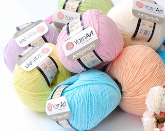 Op de afbeelding: Een verzameling YarnArt Amigurumi garenbollen in diverse pastelkleuren, waaronder lichtblauw, roze, geel, lavendel, perzik, crème en lichtgroen. Elke bol is voorzien van een papieren label met de merknaam en productdetails.