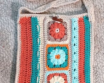 Può includere: Una borsa a tracolla all'uncinetto con una tracolla beige e un design patchwork colorato. La borsa presenta quattro quadrati con motivi floreali in tonalità arancio, blu e bianco.