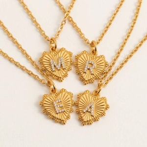 May include: Four gold-toned necklaces featuring heart-shaped pendants with a sunburst texture. Each pendant is centred with a single capital letter M, R, E, or A, encrusted with small clear stones. The necklaces have delicate gold-toned chains.