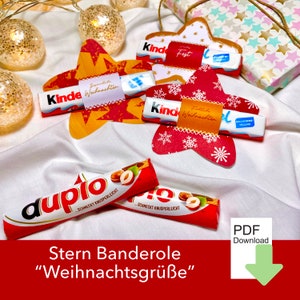 Può includere: Una composizione festosa con decorazioni a forma di stella e barrette di cioccolato Kinder. Le stelle sono rosse e dorate, con motivi a fiocco di neve e stelle. L'immagine include una barretta di cioccolato "duplo" e il testo "Stern Banderole Weihnachtsgrüße".