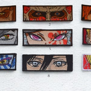 May include: Nine embroidered patches showcasing anime-style eye designs. The patches feature various colours, including red, yellow, blue, and grey. Each patch is rectangular with a black border, offering a range of expressions and styles.